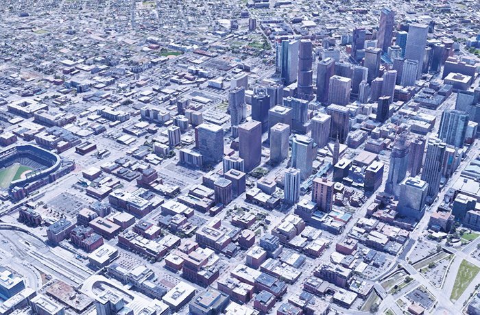 Aerial view of a dense urban cityscape with numerous tall buildings clustered together, a sports stadium visible on the left, and an intricate network of roads and smaller structures throughout the area.