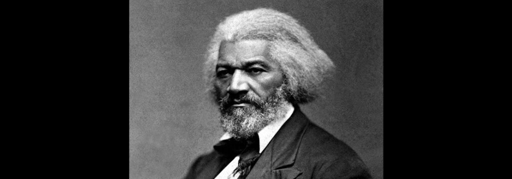 A black-and-white portrait of an older man with white hair and a full beard, dressed in a suit with a tie, looking directly at the camera with a serious expression.